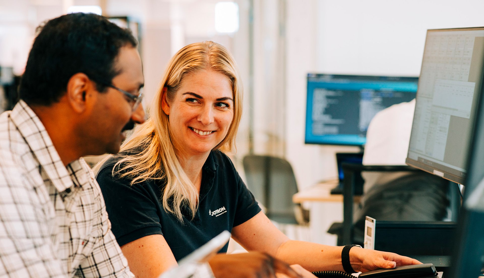Two Jotron employees in front of a PC, illustrating safety and cyber security.