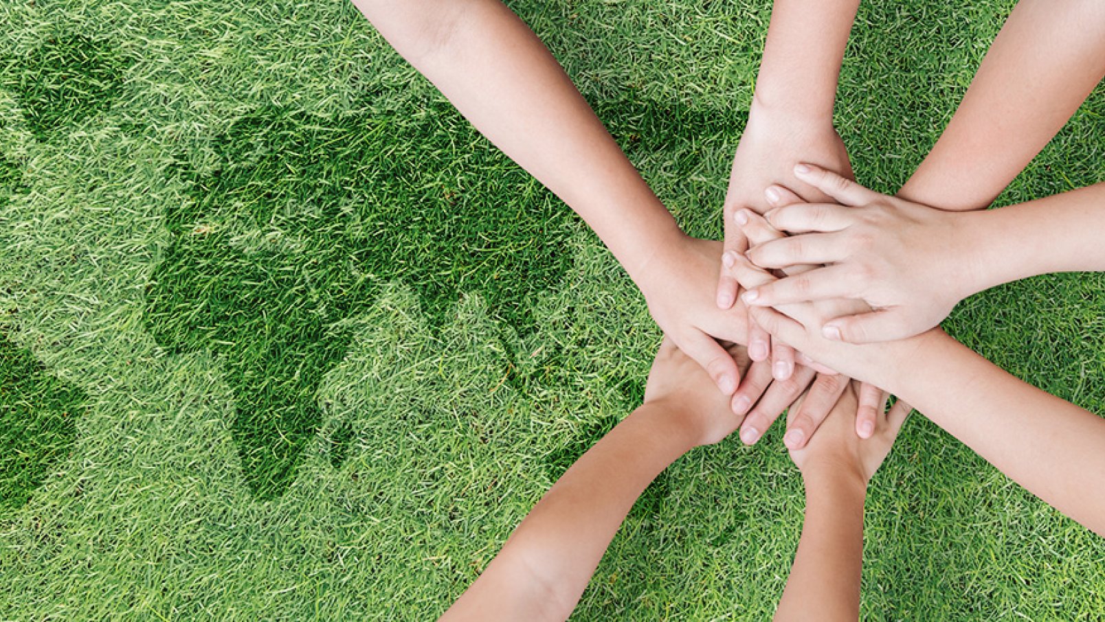 A pile of hands laying on a lawn with an embedded shape of a world map.