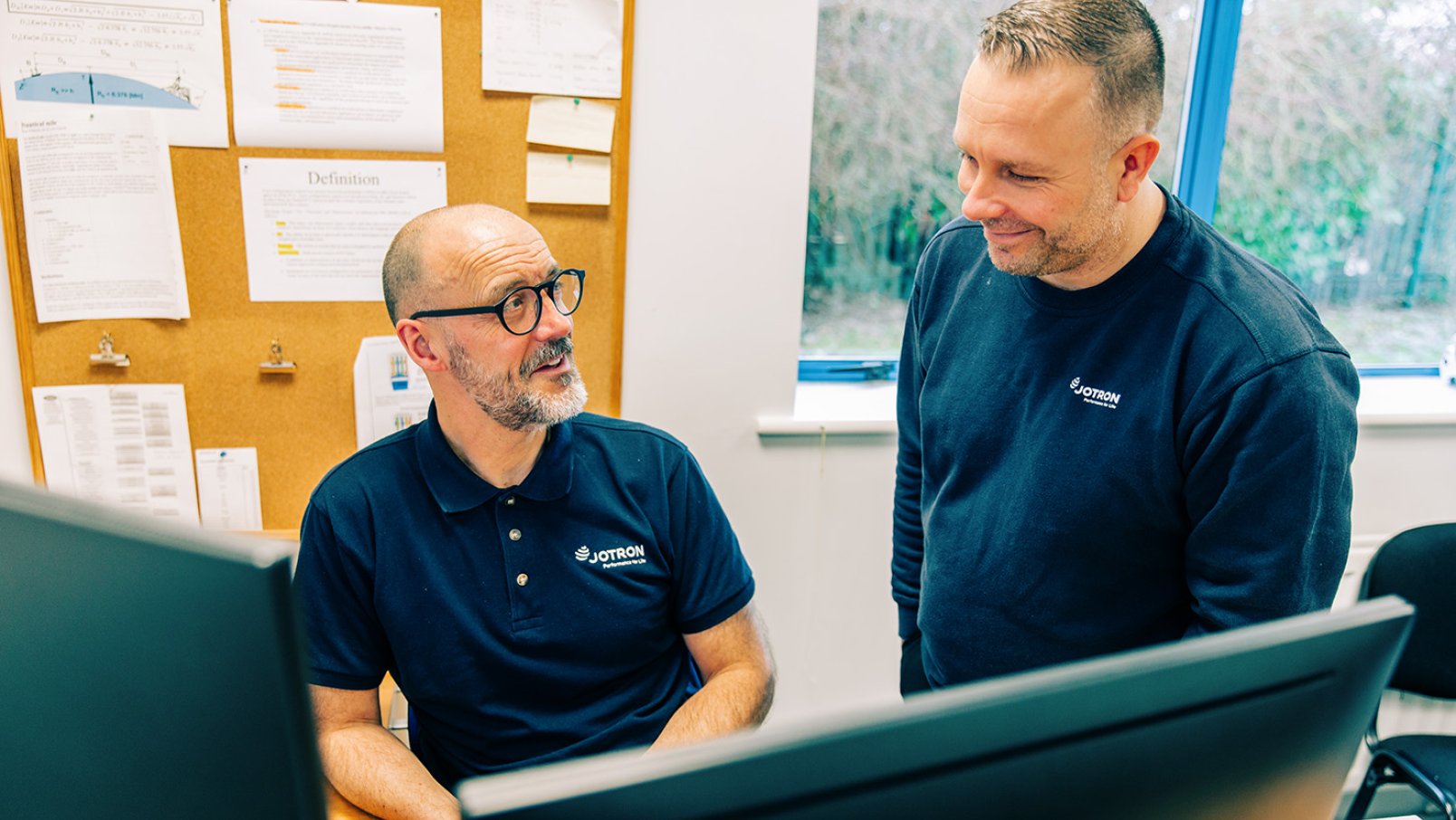 Two Jotron employees discussing in front of the PCs.