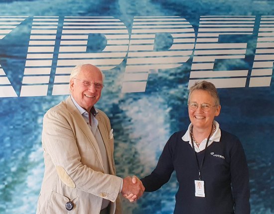 Erik Mustad, Owner, Skipper and Merete Berdal, CEO, Jotron AS shaking hands in front of a blue backwall with a large Skipper logo Erik Mustad, Owner, Skipper and Merete Berdal, CEO, Jotron AS shaking hands in front of a blue backwall with a large Skipper logo