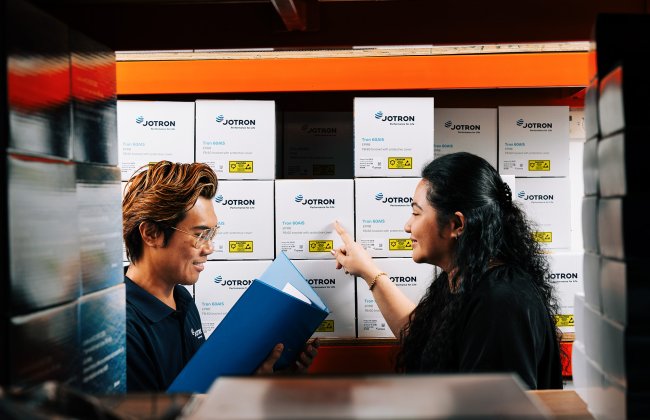 Two employees standing in front of a shelf with Jotron products. Two employees standing in front of a shelf with Jotron products.