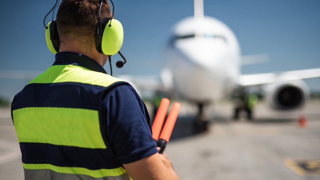 Airport worker with headphones observing a commercial jet and waiting for signaling.