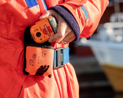 A fisherman pulls the PLB out of its carrying case, which is fastened to his belt.