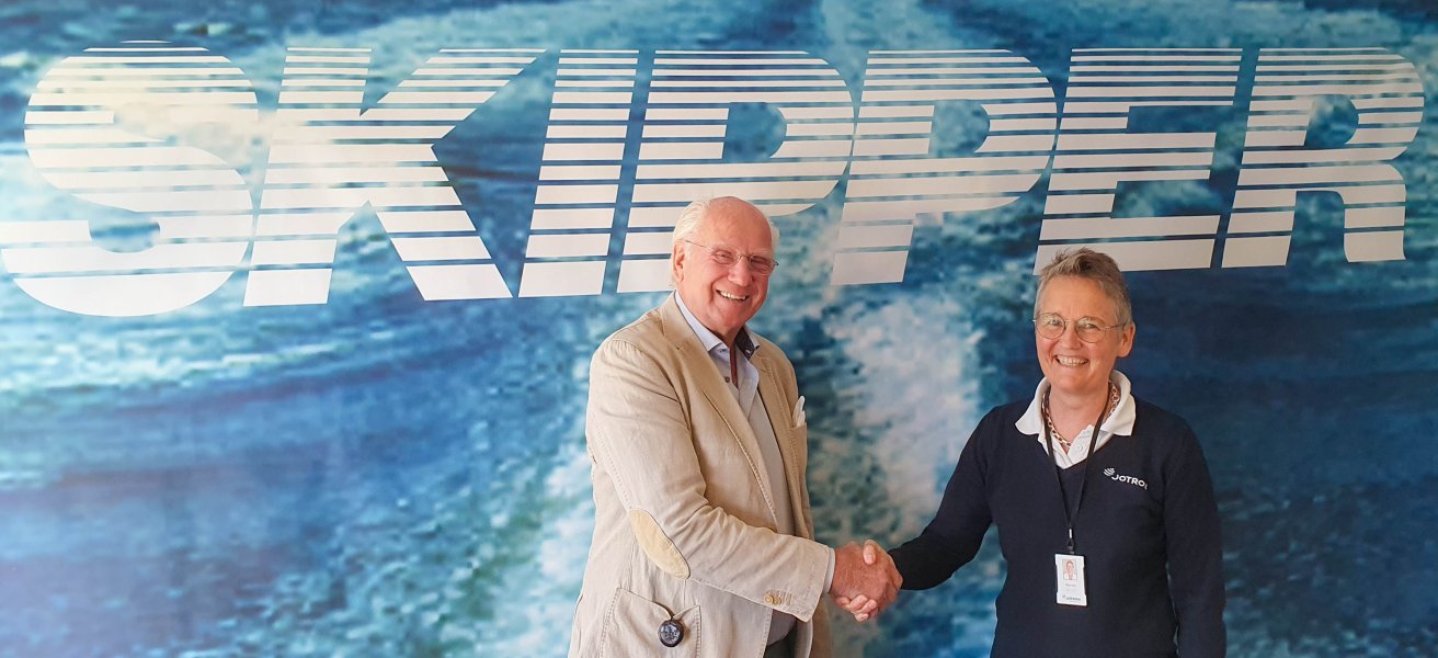 Erik Mustad, Owner, Skipper and Merete Berdal, CEO, Jotron AS shaking hands in front of a blue backwall with a large Skipper logo