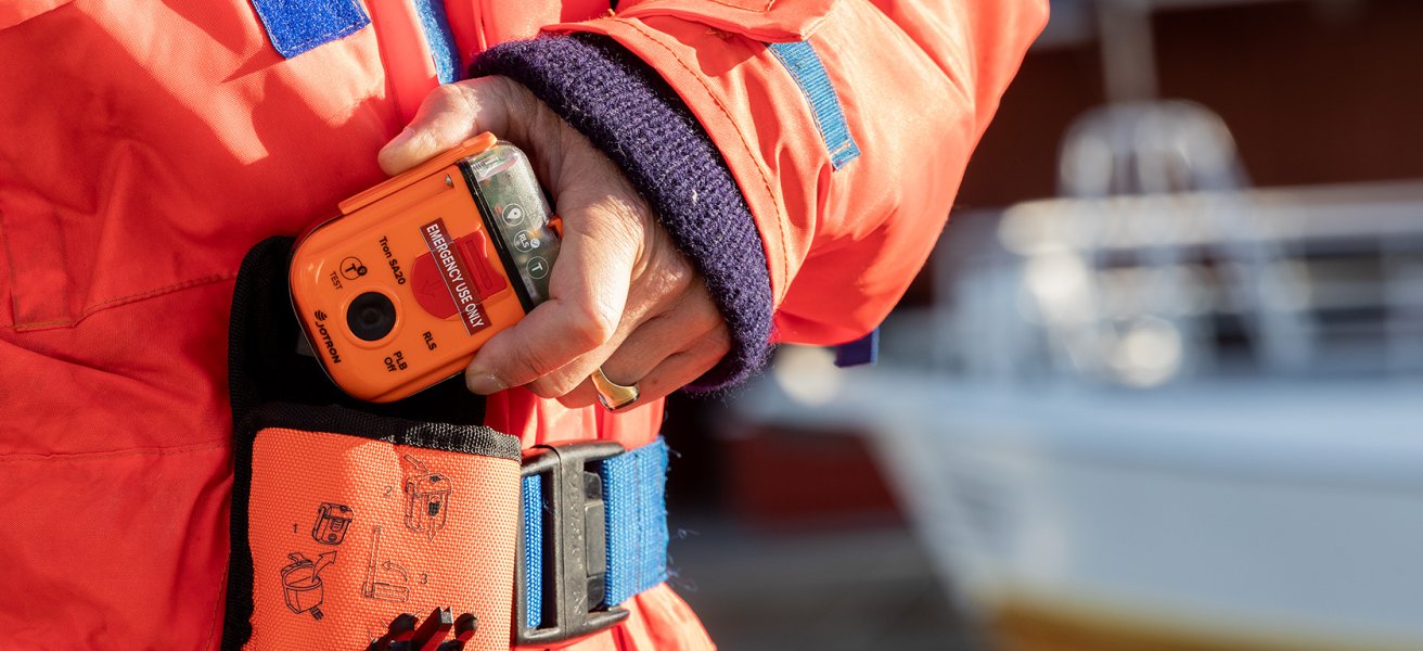 A fisherman pulls the PLB out of its carrying case, which is fastened to his belt.