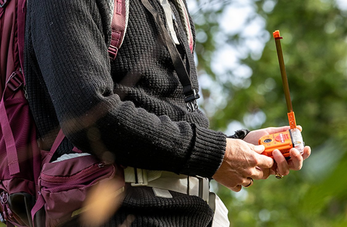 A hiker holding a Tron SA20 PLB in his hand.