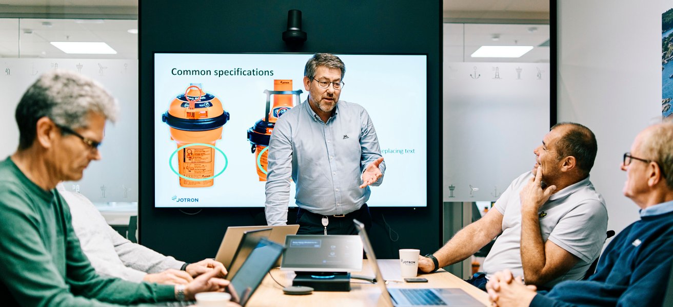 5 Jotron employees in a meeting room discussing EPIRB specifications.